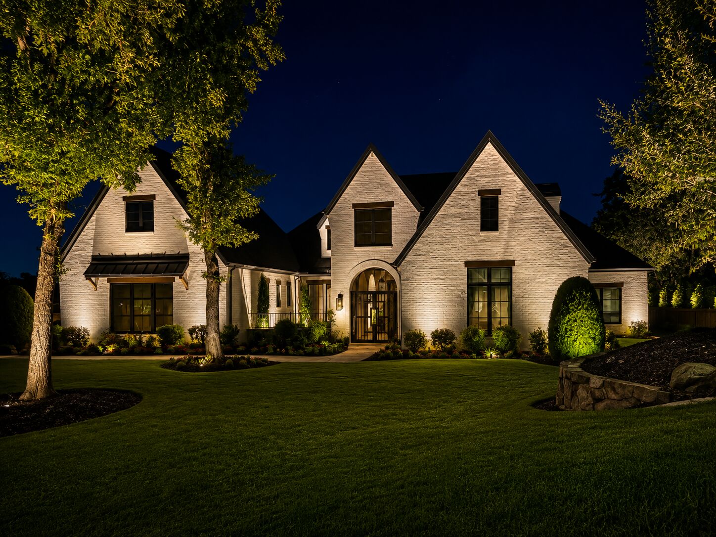 Luxury white-brick Dallas-area home with architectural and landscape uplighting at night